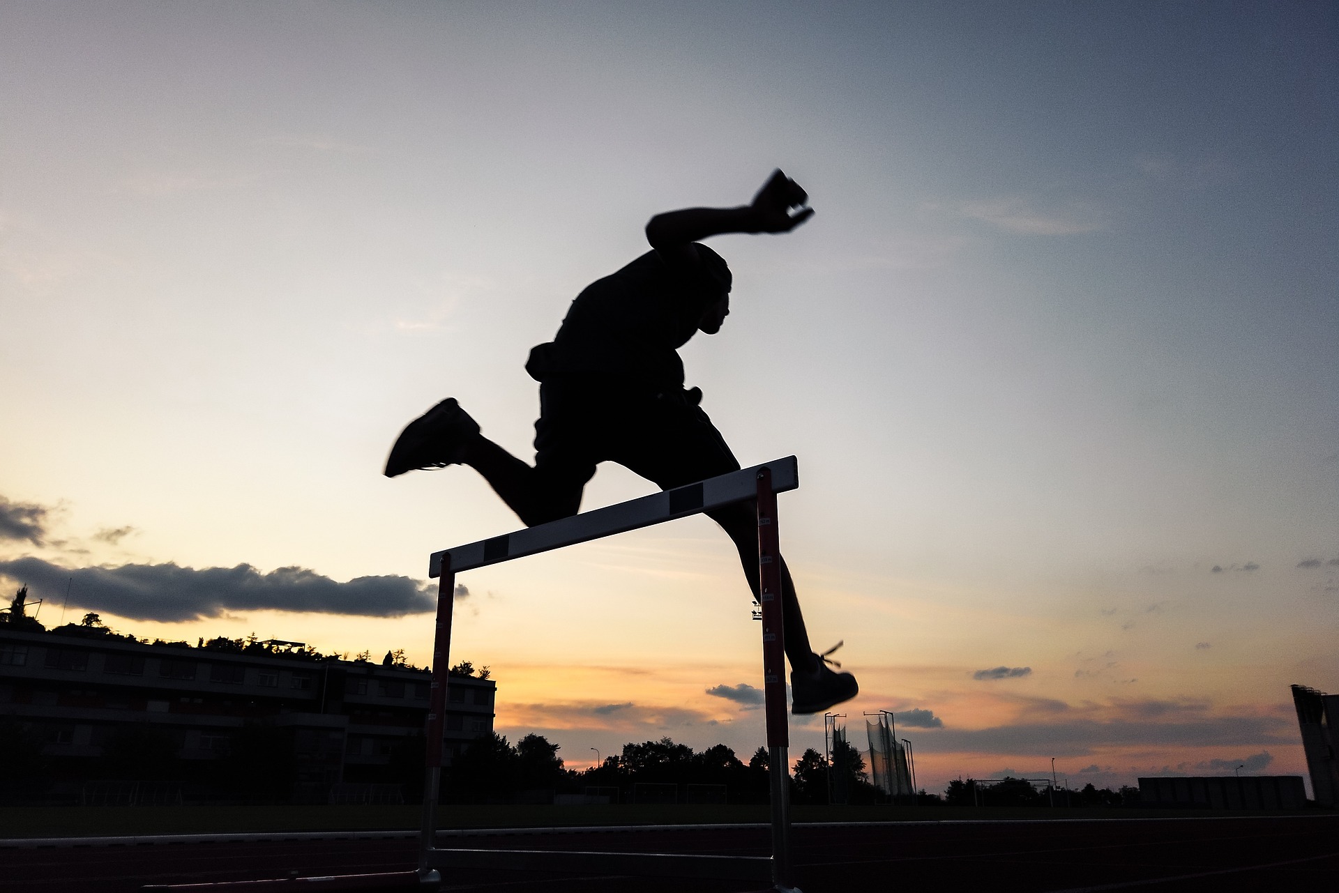 Person springt in der Dämmerung über eine Hürde.